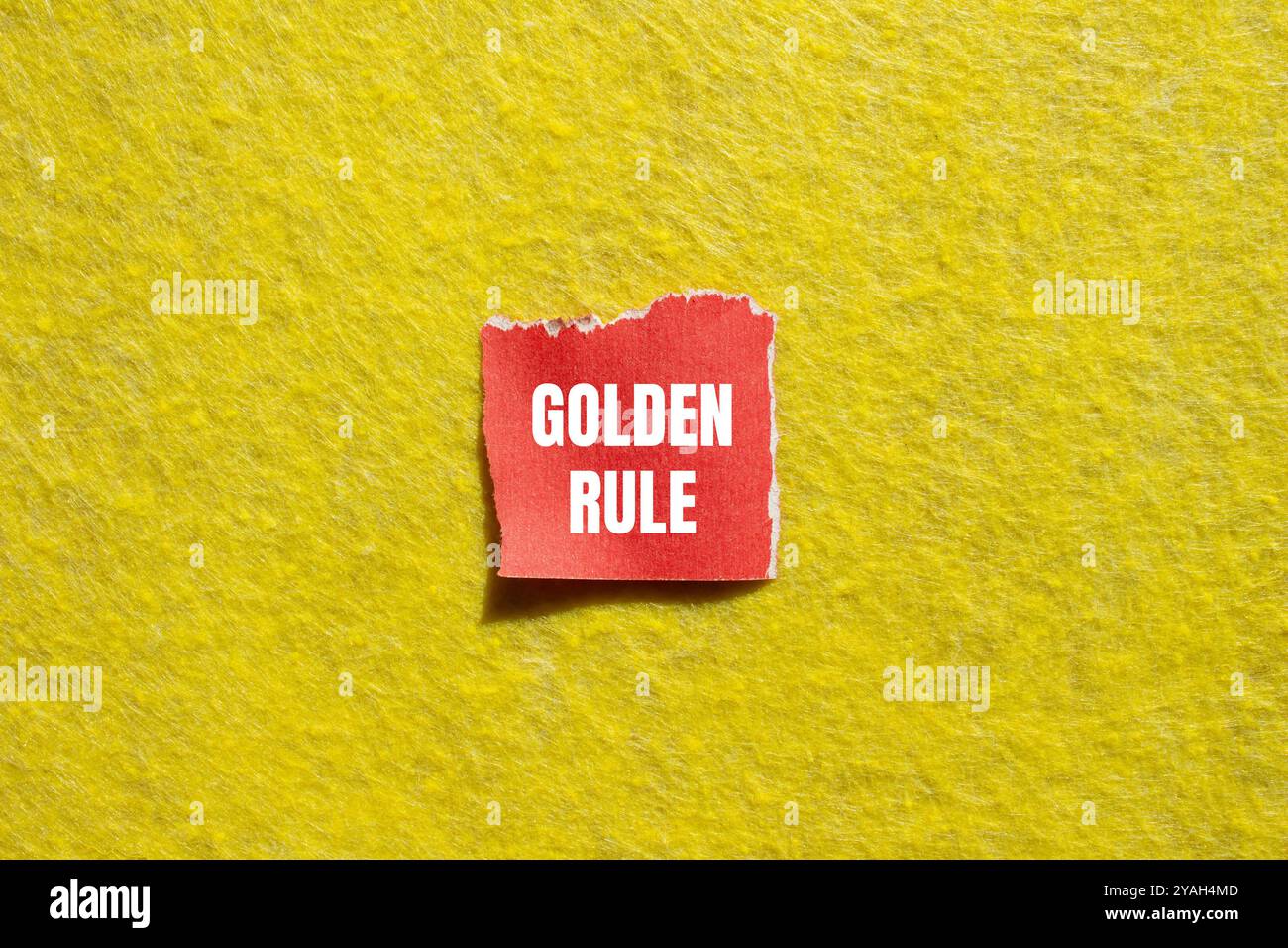 Goldene Regelnachricht auf gerissenem rotem Papierstück mit gelbem Hintergrund. Konzeptionelles goldenes Regelsymbol. Kopierbereich. Stockfoto