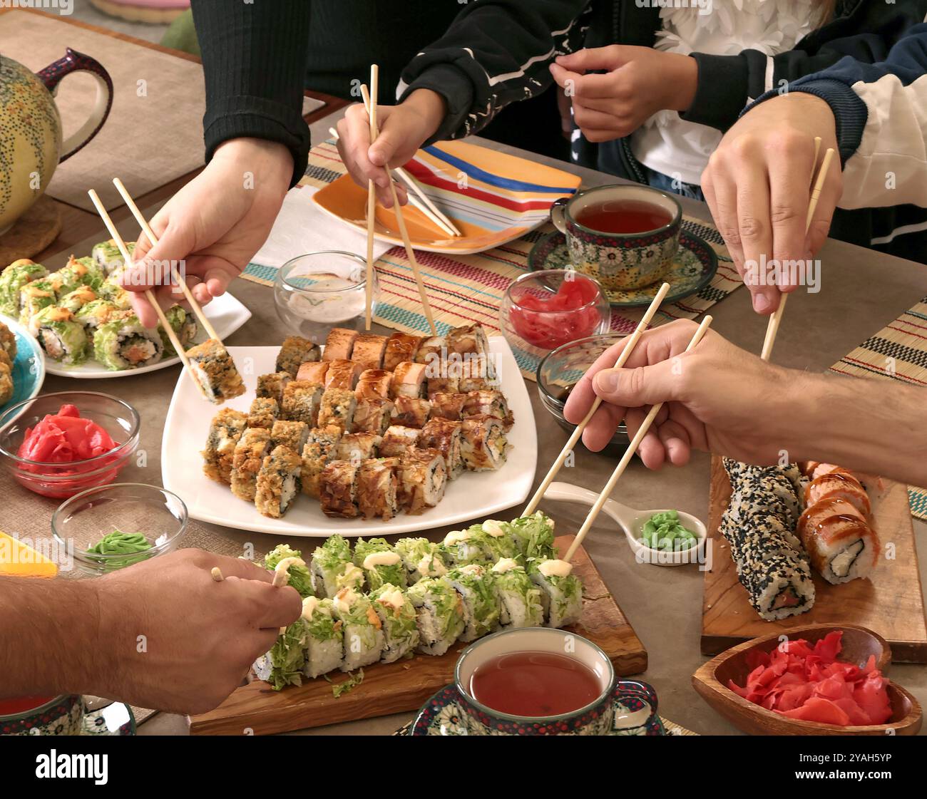 Sushi-Sets, Soße, Wasabi, Tee auf dem Feiertagstisch. Essen und traditionelle Gerichte der asiatischen Küche. Die Leute nehmen Brötchen mit Stäbchen. Tischeinstellung. Stockfoto