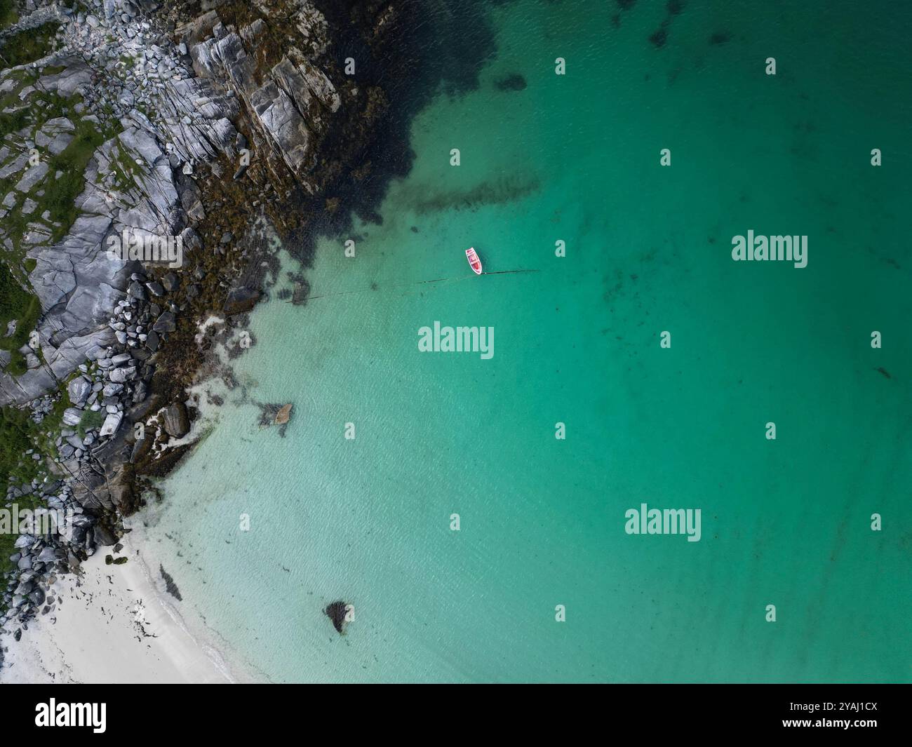 Blick aus der Vogelperspektive auf das Rote Boot, das in kristallklarem türkisfarbenem Wasser in der Nähe der felsigen Küste schwimmt Stockfoto