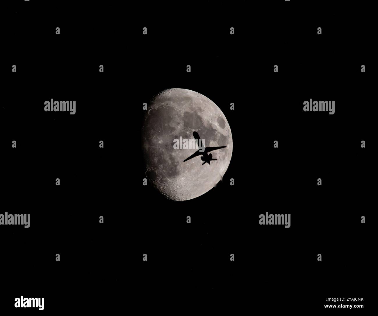 Silhouette eines Verkehrsflugzeugs, das nachts vor einem Dreiviertelmond vorbeifährt. Stockfoto
