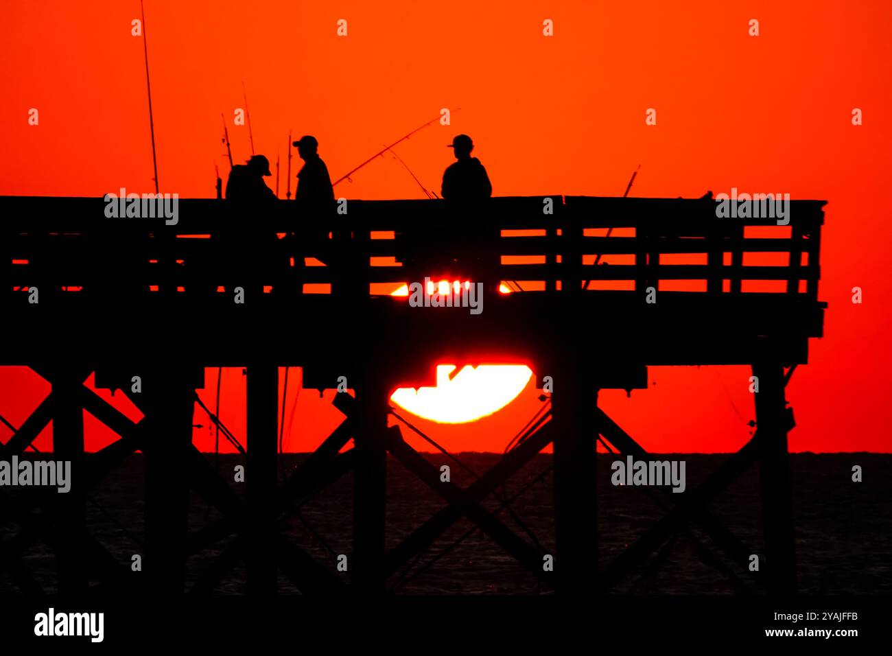 Isle Of Palms, Usa. Oktober 2024. Fisherman Silhouetten von einem dramatischen Sonnenaufgang werfen ihre Linien vor der Isle of Palms Pier am 14. Oktober 2024 in Isle of Palms, South Carolina. Klarer Himmel und warmes Wetter sind in der Prognose für das lowcountry. Quelle: Richard Ellis/Richard Ellis/Alamy Live News Stockfoto