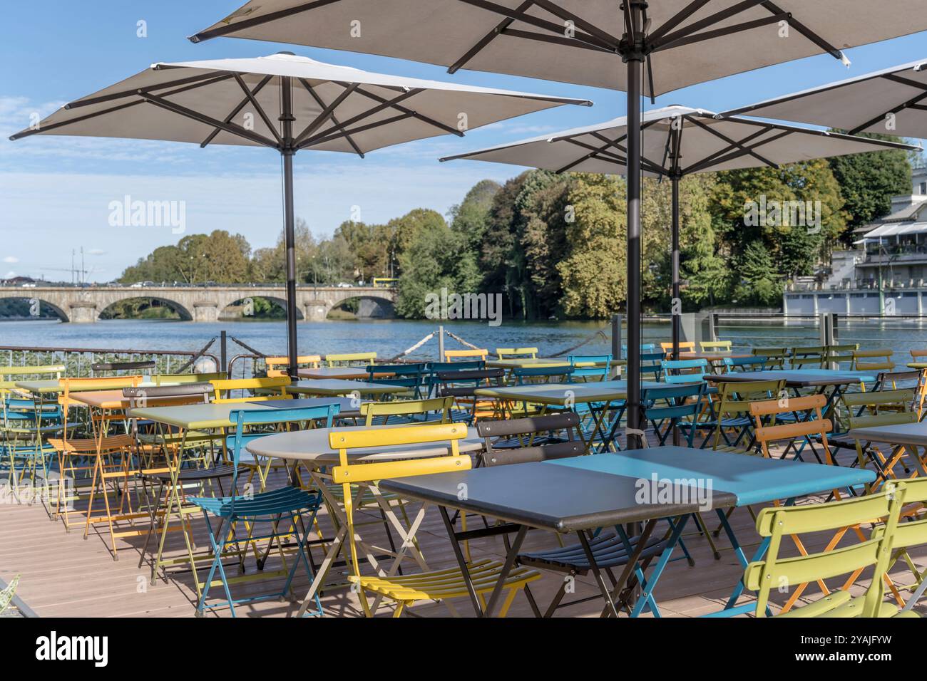 Stadtbild mit leeren Tischen und bunten Stühlen unter Sonnenschirmen im Restaurant über dem Ufer des Po, aufgenommen im hellen Herbstlicht in Turin, IT Stockfoto