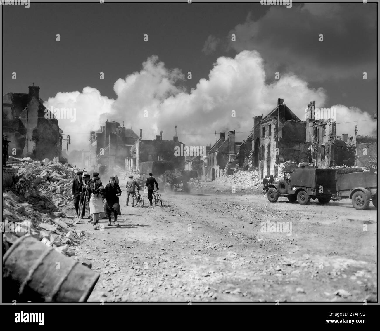 SCHLACHT DER NORMANDIE Französische Befreiung nach D-Day mitten im noch rauchenden Trümmer des befreiten Isigny-sur-Mer, passieren Zivilisten amerikanische Fahrzeuge auf dem Place Gambetta, dem heutigen Place Général de Gaulle, rechts im Hintergrund Rue Alfred Pophillat und links Rue Emile Demagny in Richtung Cherbourg N13. Juni 1944 Stockfoto