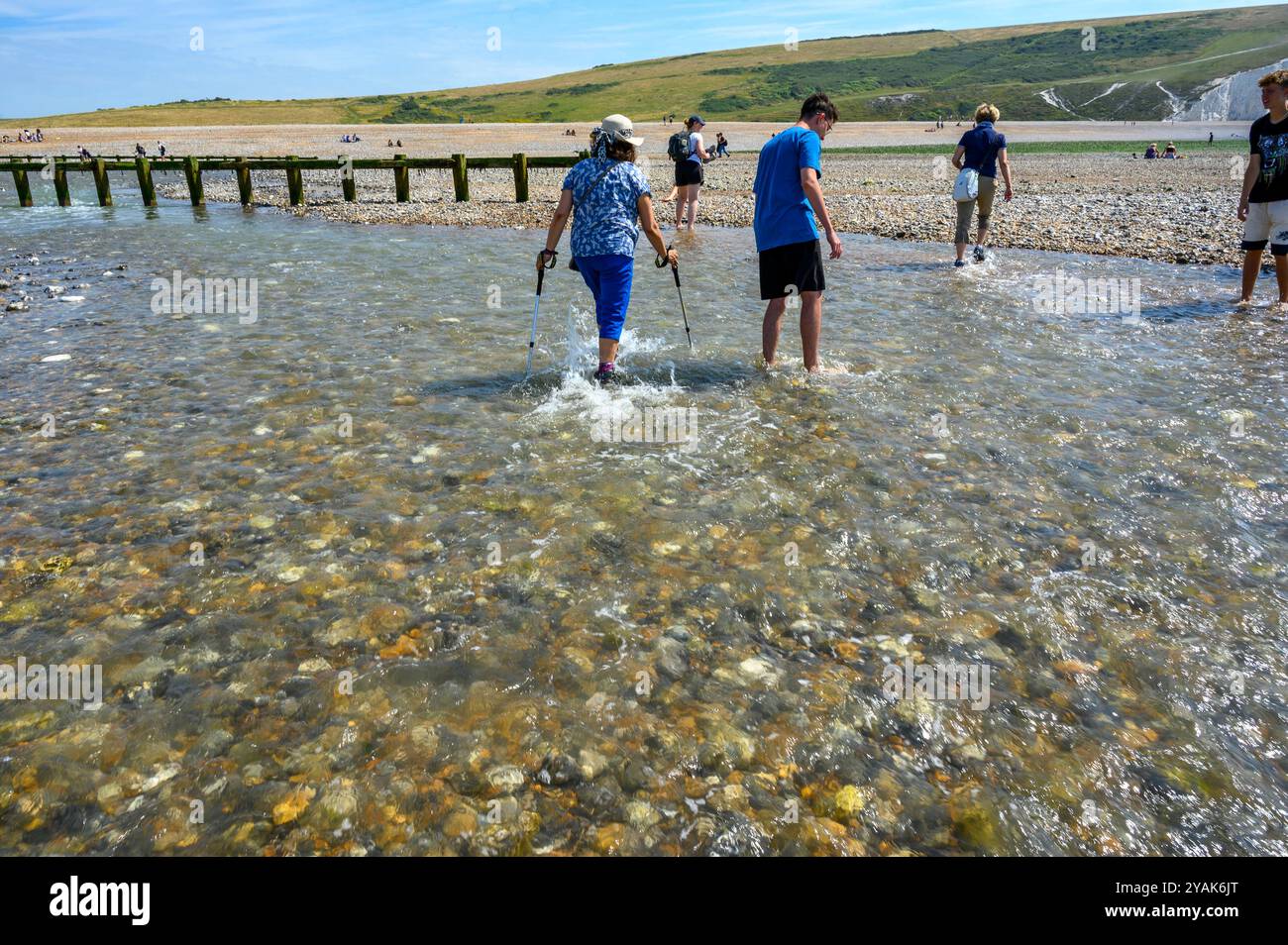 Menschen, die über den Cuckmere River waten, bei Ebtide am Cuckmere Haven zwischen Seaford Head und den Seven Sisters in East Sussex, England. Stockfoto