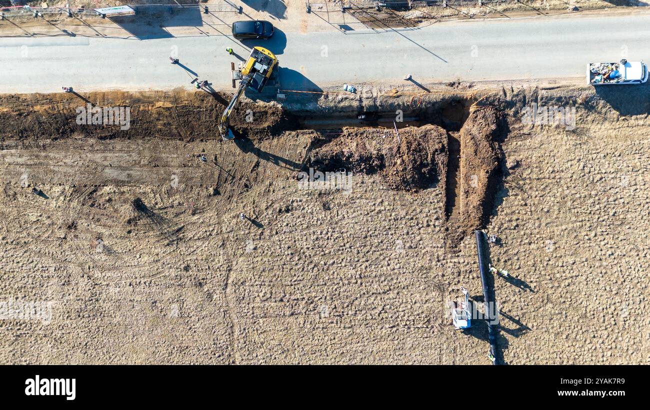 Luftaufnahme der Baustelle mit Baggern, die einen Graben für ein Rohr in der Nähe einer Straße graben. Stockfoto