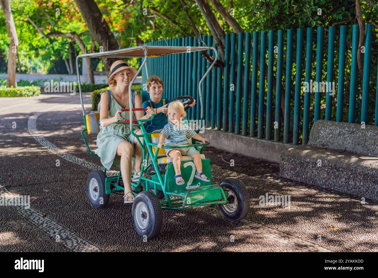 Mutter Tourist mit ihrem Kleinkind und ihren Söhnen im Teenageralter, die in einem authentischen mexikanischen Tretwagen in einem Park in Mexiko fahren. Familienabenteuer und Reisen mit Kindern Stockfoto