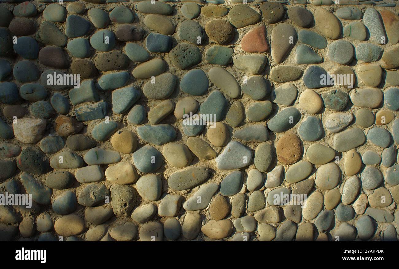 Ein fesselndes Arrangement aus glatten, bunten Flusssteinen schafft eine atemberaubende visuelle Darstellung, die wunderschön durch warmes Sonnenlicht in einem Außenbereich beleuchtet wird Stockfoto