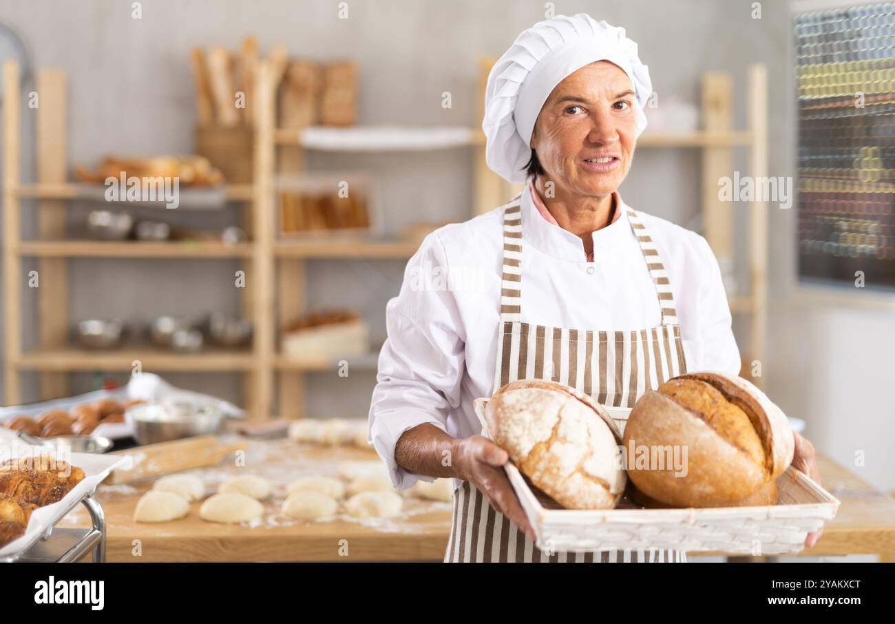 Erfolgreiche ältere Bäckerin, die ein Tablett mit frischem Brot hält Stockfoto