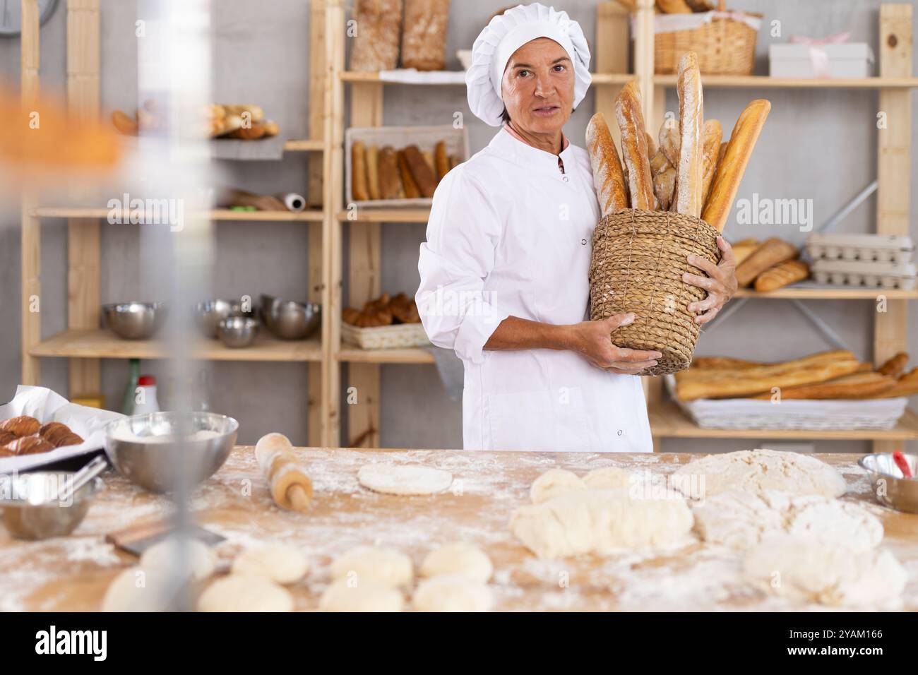 Lächelnde ältere Bäckerin, die einen Korb mit goldenen Baguettes hält Stockfoto