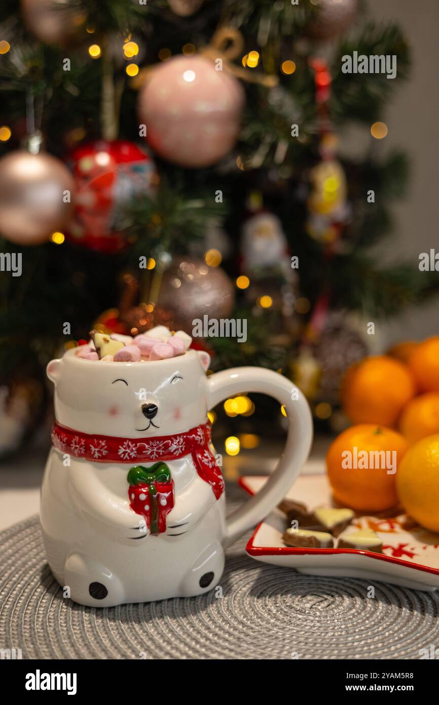 Nahaufnahme eines niedlichen Eisbärenbechers, der vor einem verzierten Weihnachtsbaum mit festlichen Ornamenten steht. Konzept von gemütlichen Winterferien und warmen Getränken Stockfoto
