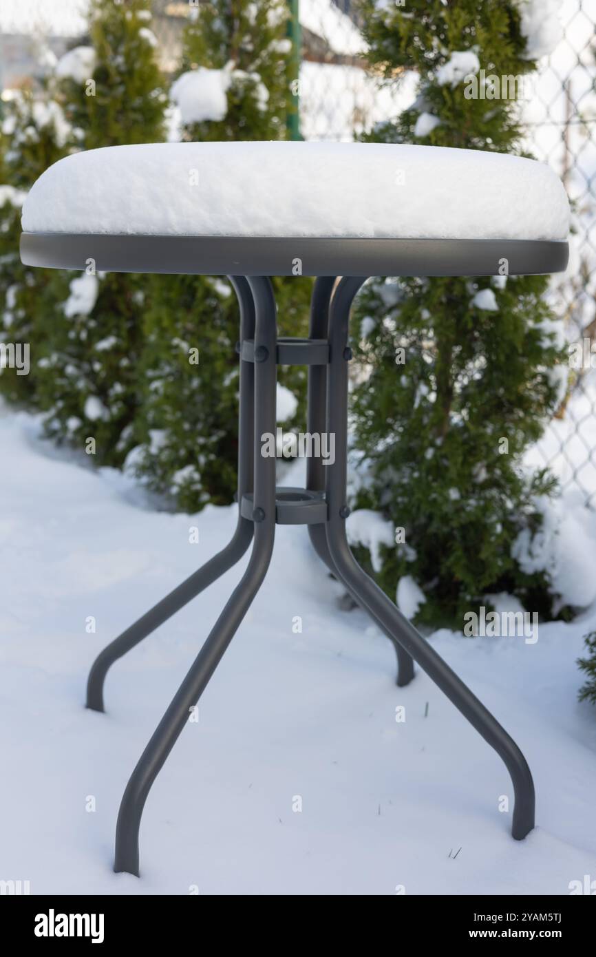 Schneebedeckter runder Tisch im Garten an einem kalten Wintertag. Konzept der Wintersaison, Gartenmöbel und schneebedecktes Wetter im Hinterhof Stockfoto