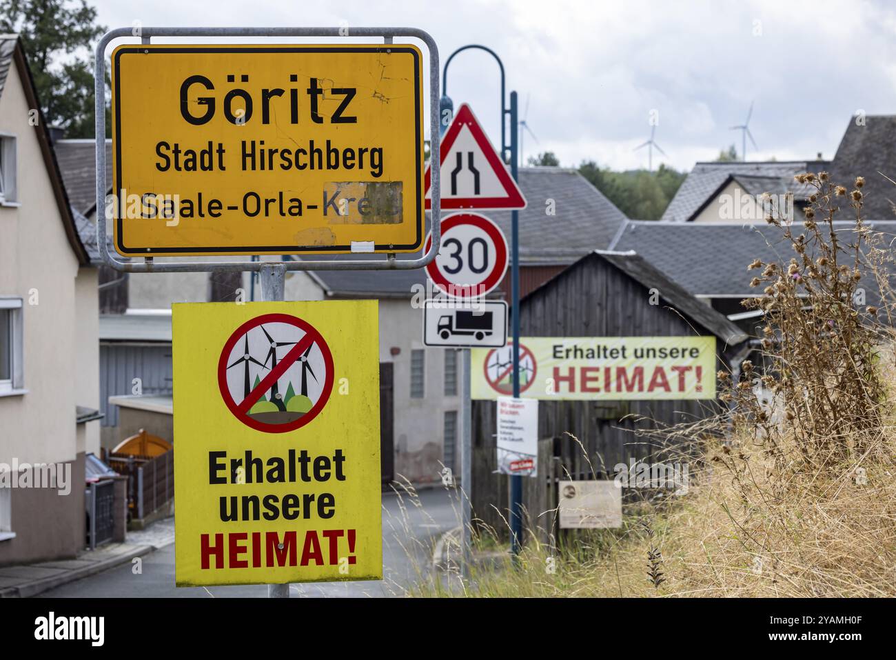 Protest gegen Windräder im ehemaligen deutsch-deutschen Grenzgebiet Thüringen-Bayern. Stadtschild mit Protestplakaten in einem ländlichen setti Stockfoto
