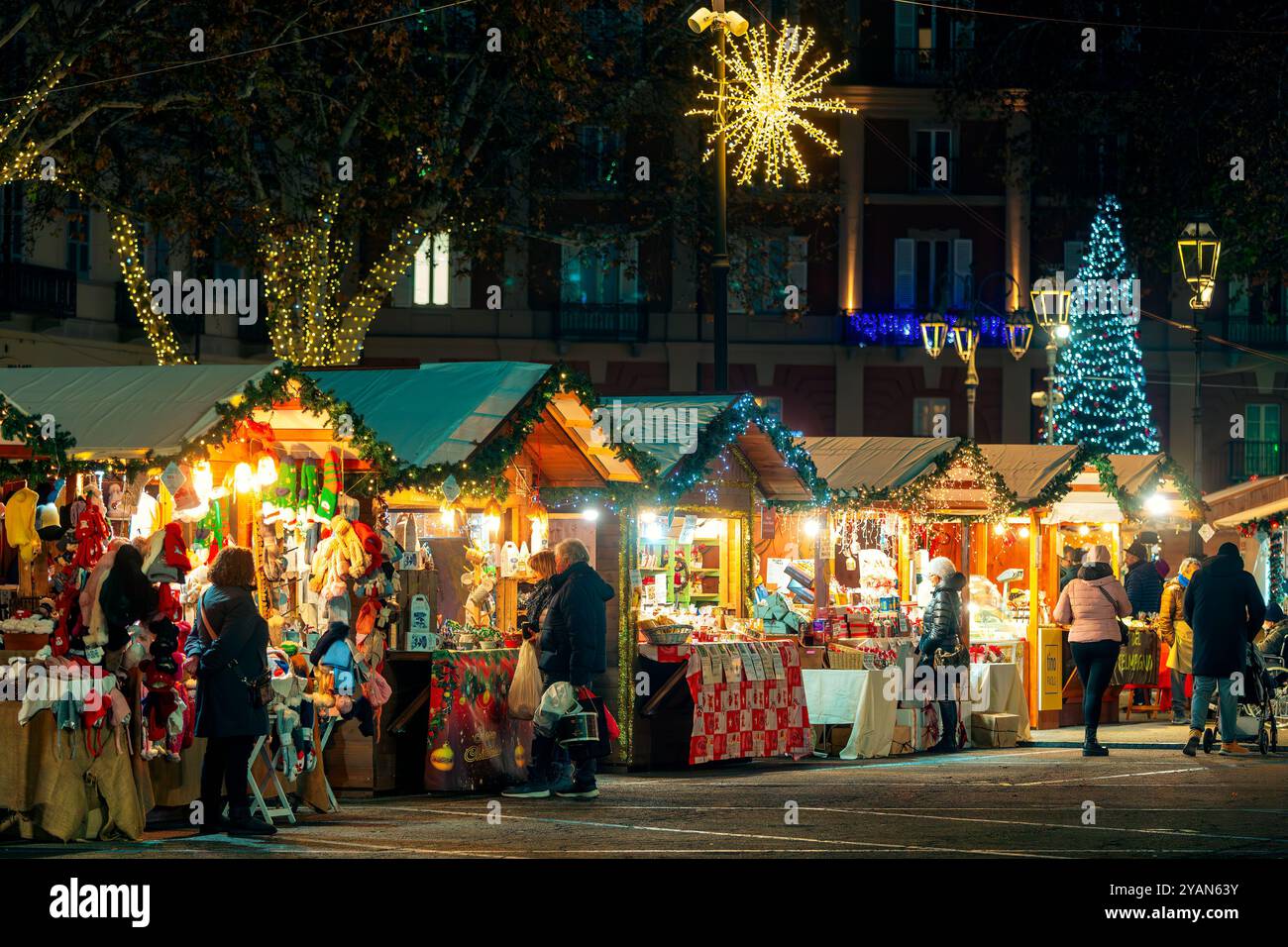 Menschen laufen entlang beleuchteten Holzkiosks auf dem Weihnachtsmarkt in Asti - einem der berühmten und beliebten jährlichen Märkte in Italien. Stockfoto