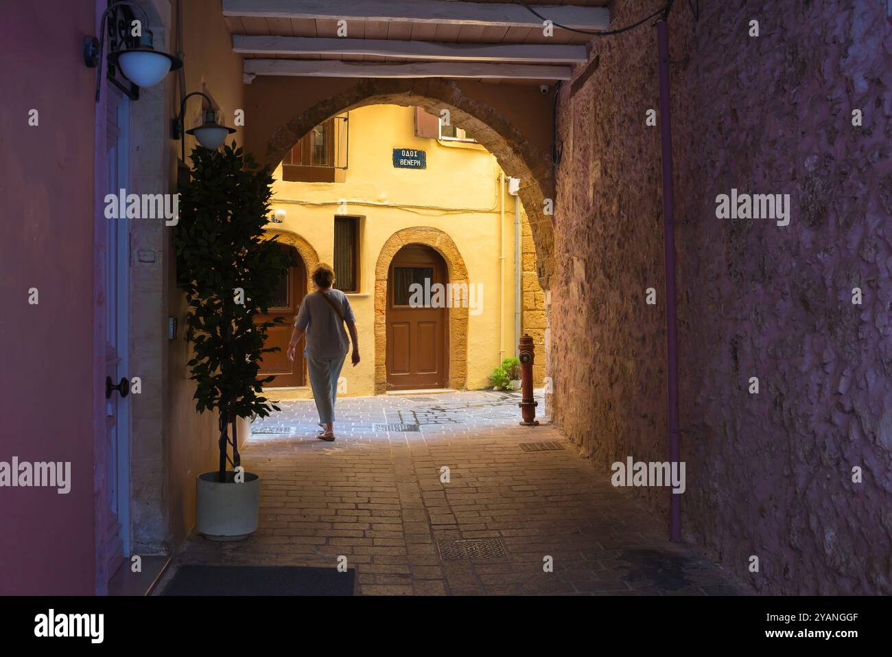 Senior weibliche Touristen, Rückansicht einer einzigen Frau mittleren Alters, die durch eine farbenfrohe Gasse in der malerischen Altstadt von Chania in Kreta, Griechenland, spaziert. Stockfoto