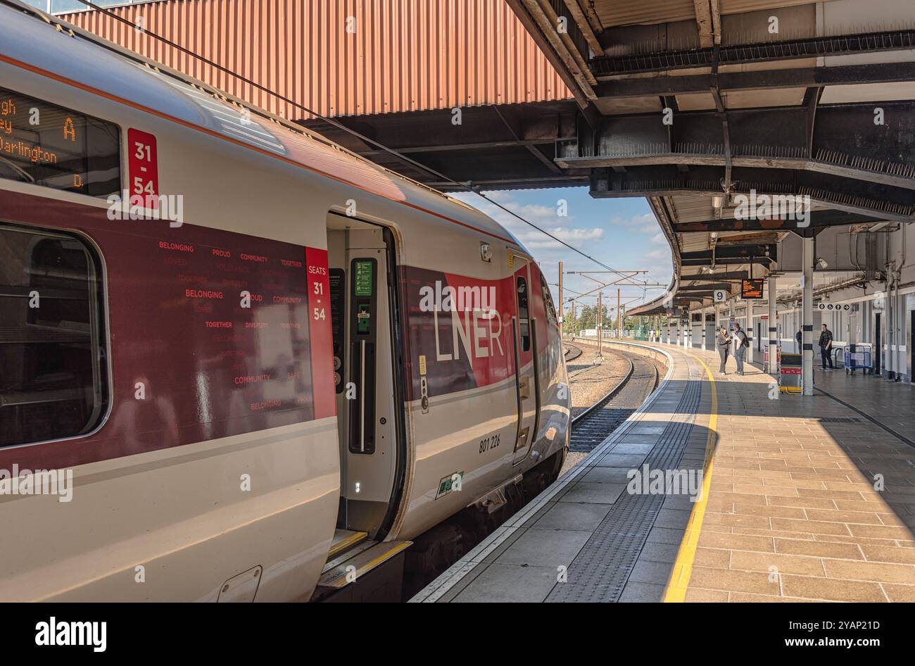 Ein Zug steht an einem Bahnsteig mit offener Tür. Der Bahnsteig biegt sich in die Distanz, und die Passagiere befinden sich auf dem Bahnsteig. Stockfoto