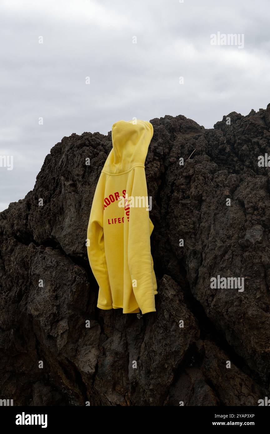 Ein leuchtend gelber Rettungsschwimmer-Hoodie hängt an dunklen Vulkanfelsen in den natürlichen Pools von Porto Moniz Stockfoto