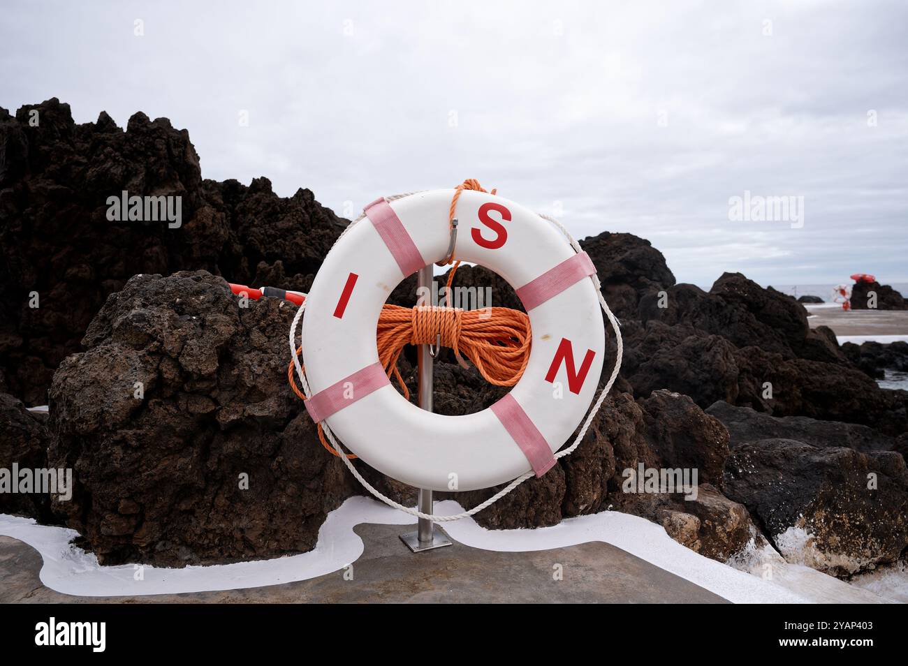 Ein Rettungsschirm mit orangefarbenem Seil steht an den natürlichen Pools von Porto Moniz vor dunklen vulkanischen Felsen Stockfoto