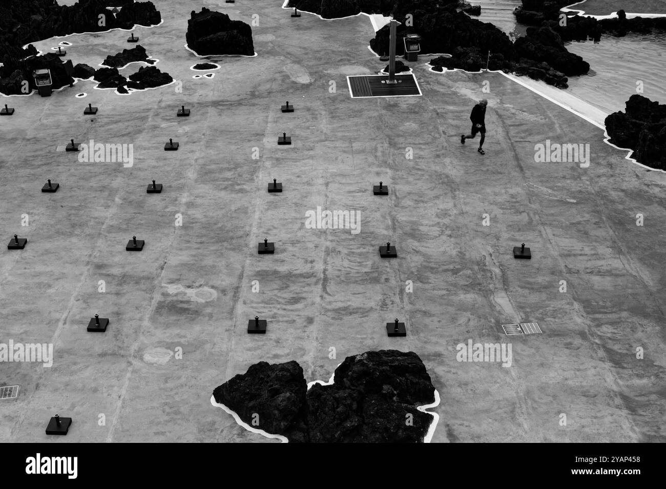 Einsame Figur spaziert an den Reihen der Sonnenschirmbasen in den natürlichen Pools von Porto Moniz Stockfoto