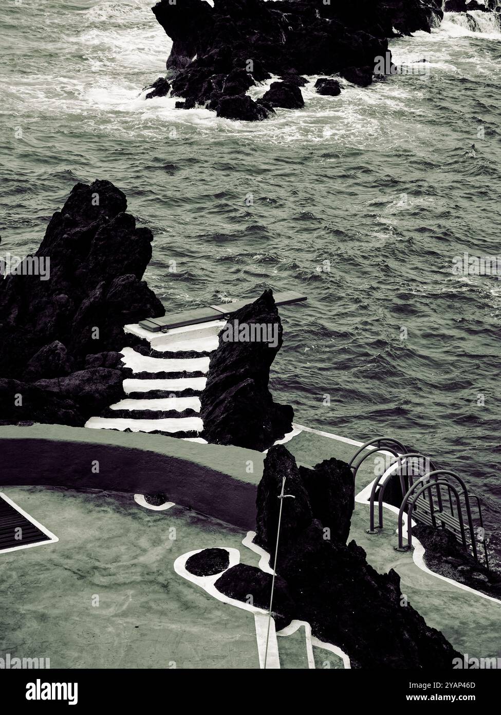 Schwarzweiß-Aufnahme von Porto Moniz, wo der wilde Ozean auf künstliche Treppen und Tauchbretter an Madeiras rauer Küste trifft Stockfoto
