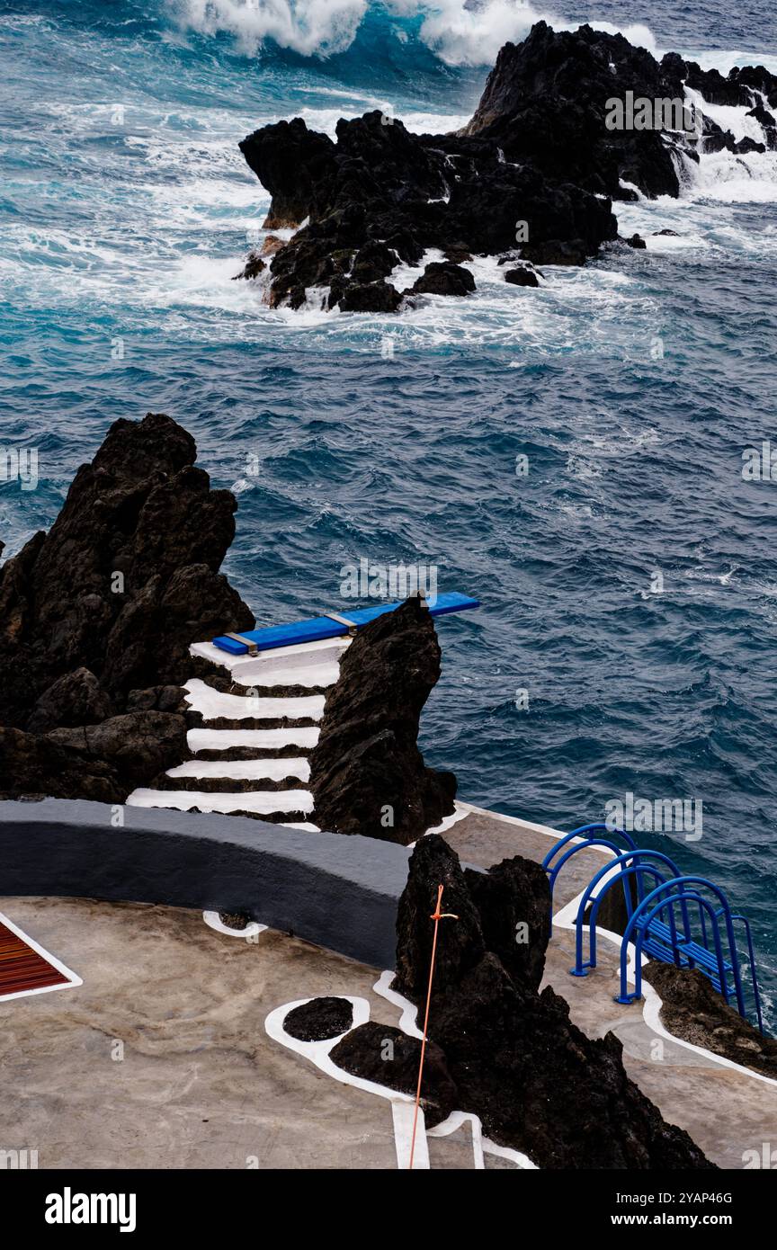Wellen schlagen gegen die vulkanischen Felsen und ein blaues Tauchbrett an den natürlichen Pools von Porto Moniz Stockfoto