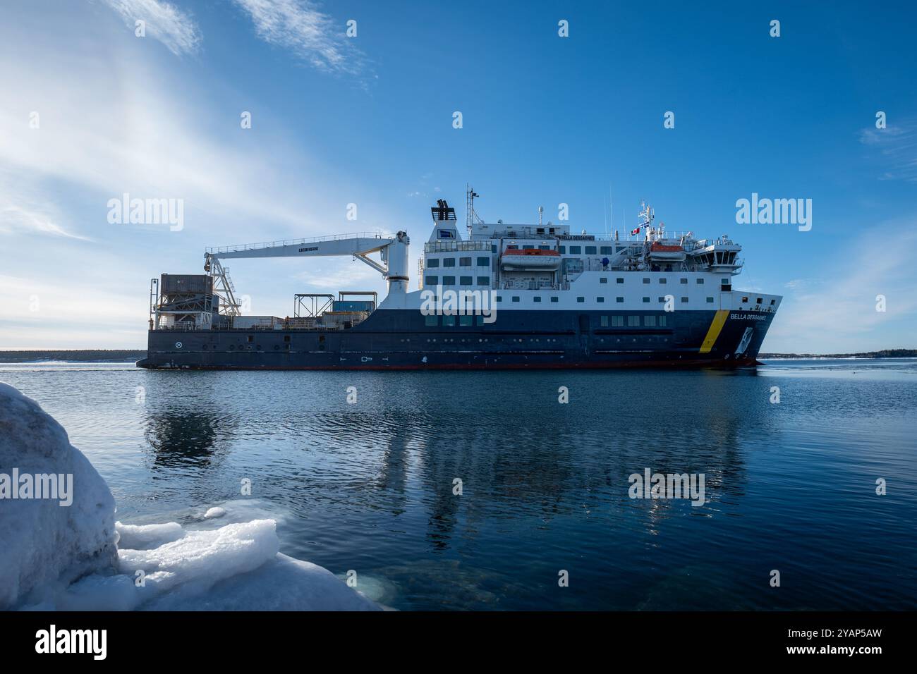 Anticosti Island, Québec, Kanada – 7. Januar 2024: Ein großes Frachtschiff mit mehreren Etagen, Kran und Containern segelt im Ozean und kommt an einem Po an Stockfoto