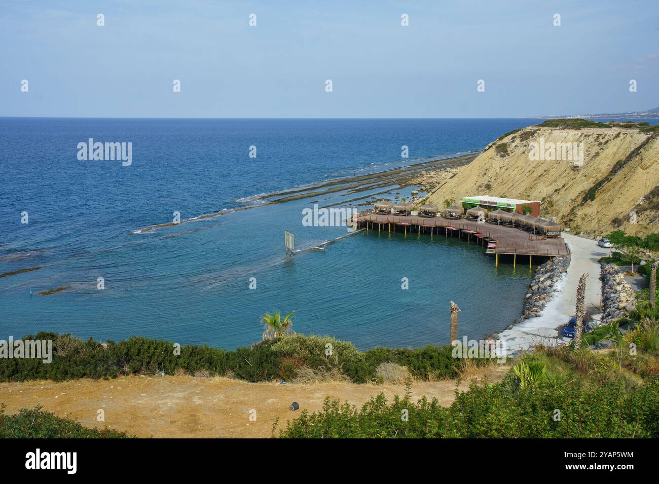 Die Wellen schlagen sanft gegen den verwitterten Pier, wo die Besucher verweilen und die Wärme der Sonne genießen, während sie die atemberaubende aussicht auf das Meer genießen und die Umgebung genießen Stockfoto