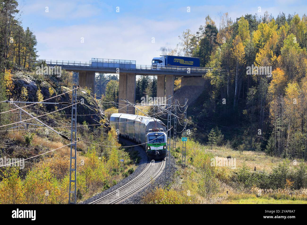 Der zweistöckige Personenzug der VR Group Intercity fährt unter der Brücke, während der Sattelauflieger von Iveco auf der Brücke fährt. Salo, Finnland. Oktober 2024. Stockfoto