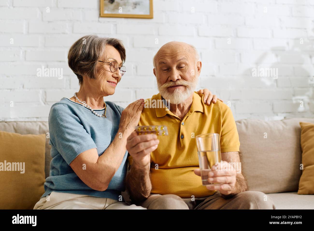 Eine ältere Frau tröstet ihren Mann sanft, während er sich auf die Einnahme seiner Medikamente vorbereitet. Stockfoto