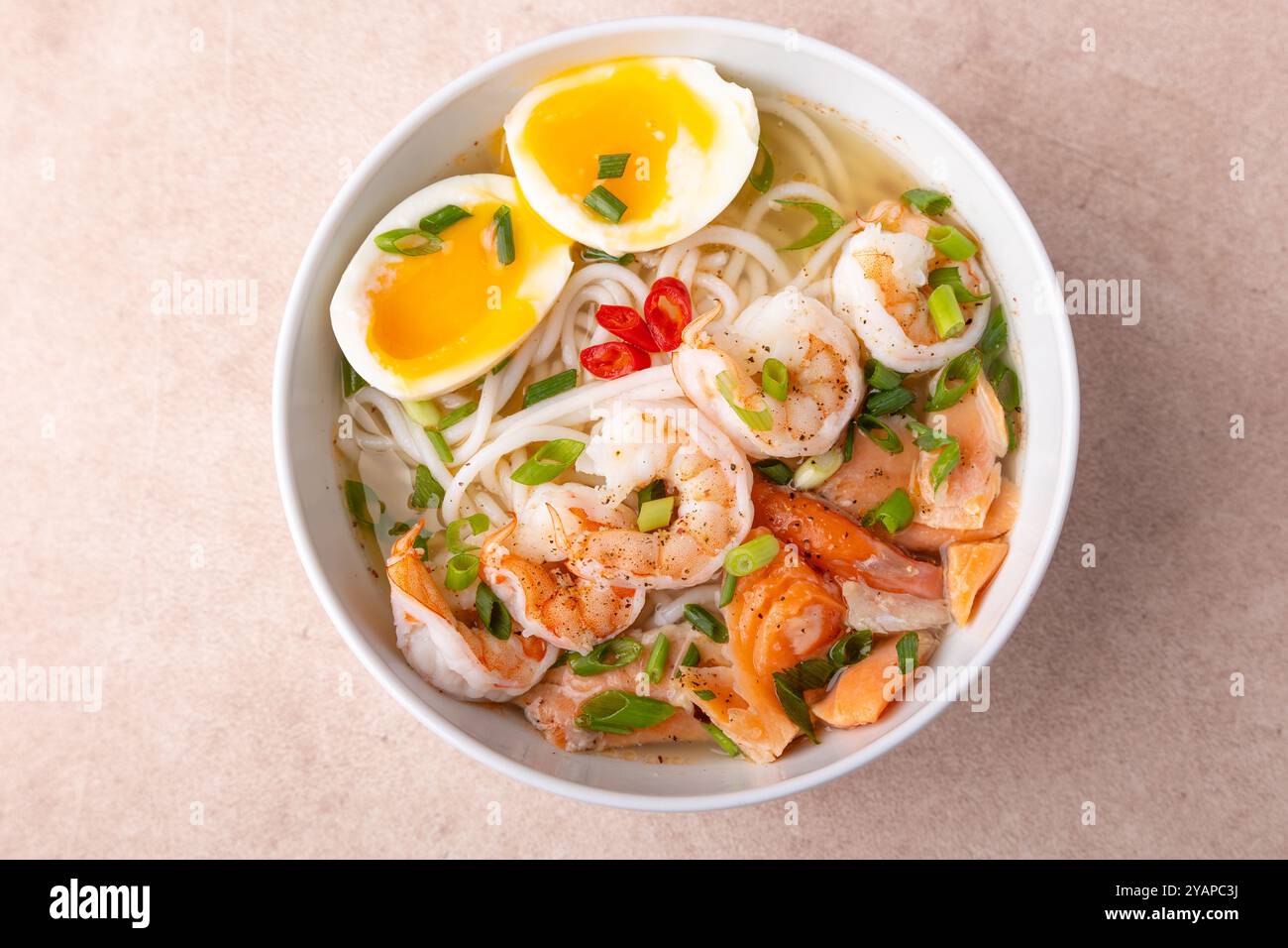 Asiatisches Gericht mit Brühe, Nudeln, Tigergarnelen, Fisch, Ei und grünen Zwiebeln. Traditionelle asiatische Suppe auf einem weißen, tiefen Teller. Selektiver Fokus, Nahaufnahme. Stockfoto