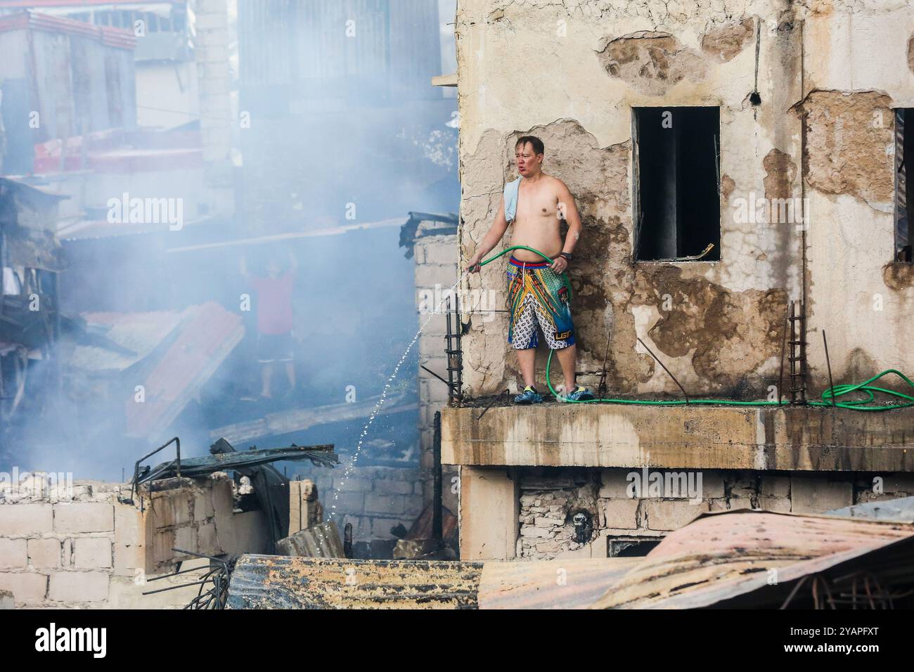 Manila, Philippinen. Oktober 2024. Ein Bewohner benutzt einen Wasserschlauch in seinem verkohlten Haus nach einem Brand in einem Slum-Gebiet in Manila, den Philippinen, am 15. Oktober 2024. Quelle: Rouelle Umali/Xinhua/Alamy Live News Stockfoto