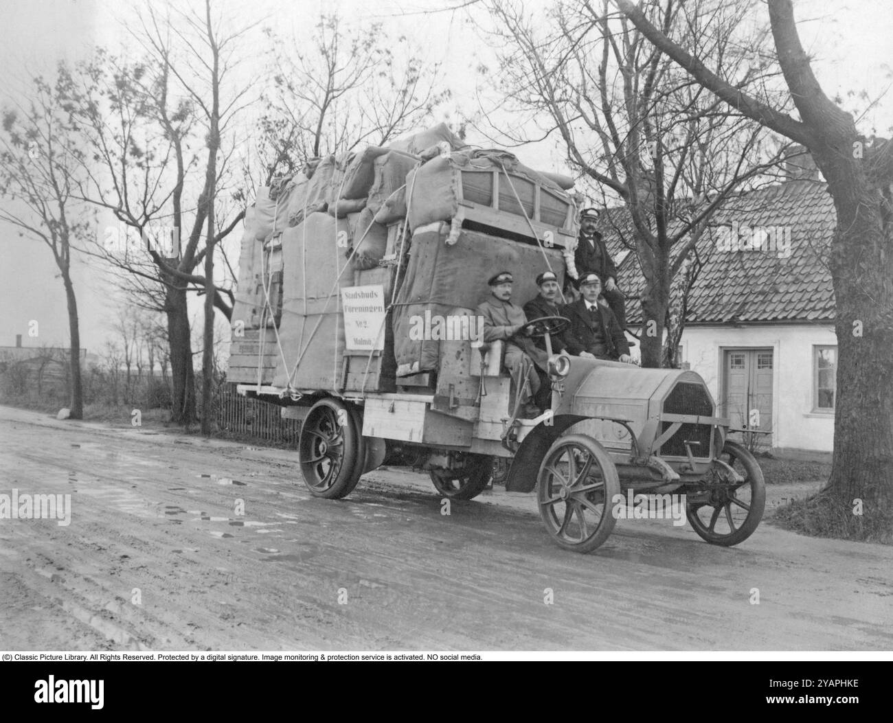 Ein voll beladener LKW. Vor einem Haus steht ein Lastwagen der Firma Malmö Stadsbud und ist voll beladen mit zu transportierenden Haushaltsgütern. Möbel und Kisten sind gut verpackt und mit Seilen verzurrt. Der alte Ford-Lkw hat massive Gummiräder und Platz für drei Personen, die auf dem Sitz sitzen. Ein Schild auf dem LKW steht für den Namen des Unternehmens, dem die Umzugsgesellschaft Stadsbudsföreningen Nr. 2 Malmö 1920s gehört Stockfoto