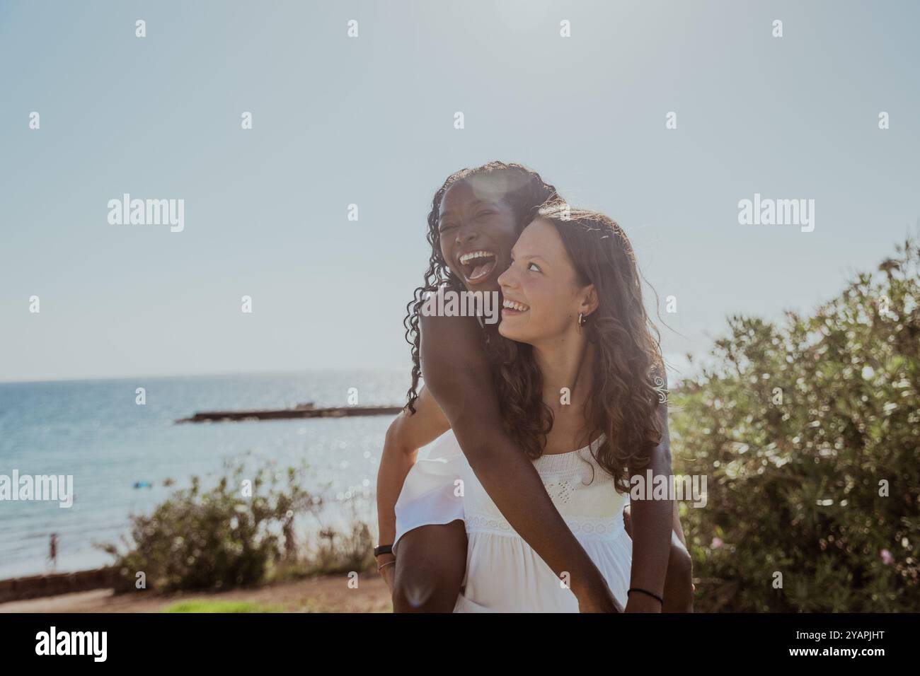 Zwei Frauen lächeln und umarmen sich am Strand. Die Szene ist glücklich und fröhlich Stockfoto