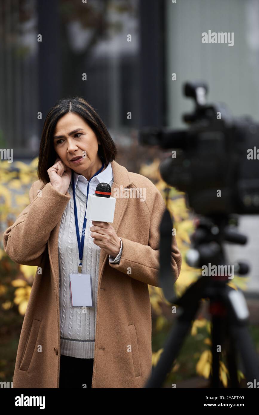 Eine fokussierte multirassische Journalistin hält ein Mikrofon, während sie sich auf ein Outdoor-Nachrichtensegment vorbereitet. Stockfoto