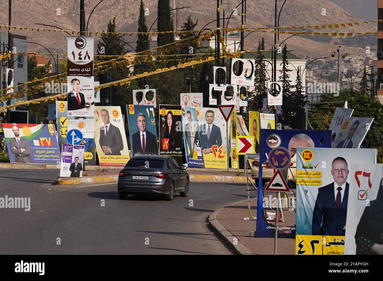 Ein Auto fährt in einem Kreisverkehr vorbei an Wahlbändern für Kandidaten vor den Wahlen zum Kurdischen Regionalparlament in Duhok, Irak. Stockfoto