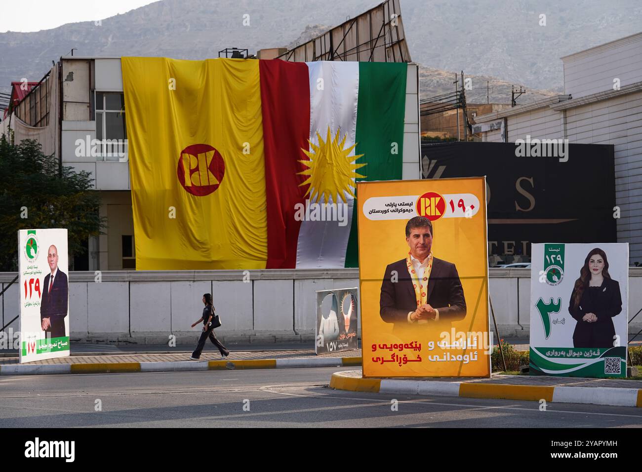 Eine junge Frau läuft an Wahlbändern der Patriotischen Union Kurdistans (PUK) und dem Bild des Vizepräsidenten der Partei Nechirvan Barzani vor den Wahlen zum Kurdischen Regionalparlament in Duhok im Irak vorbei. Stockfoto