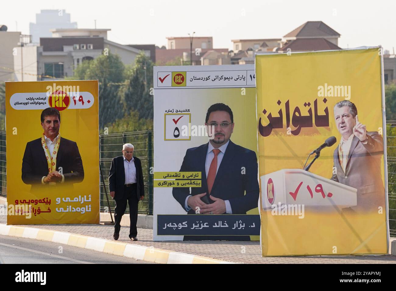 Ein Mann läuft an Wahlbändern des Kandidaten der Kurdischen Demokratischen Partei (KDP/PDK) und anderen vorbei, die Bilder der Vizepräsidenten der Partei Nechirvan Barzani und Masrour Barzani vor den Wahlen zum Kurdischen Regionalparlament in Duhok im Irak zeigen. Stockfoto