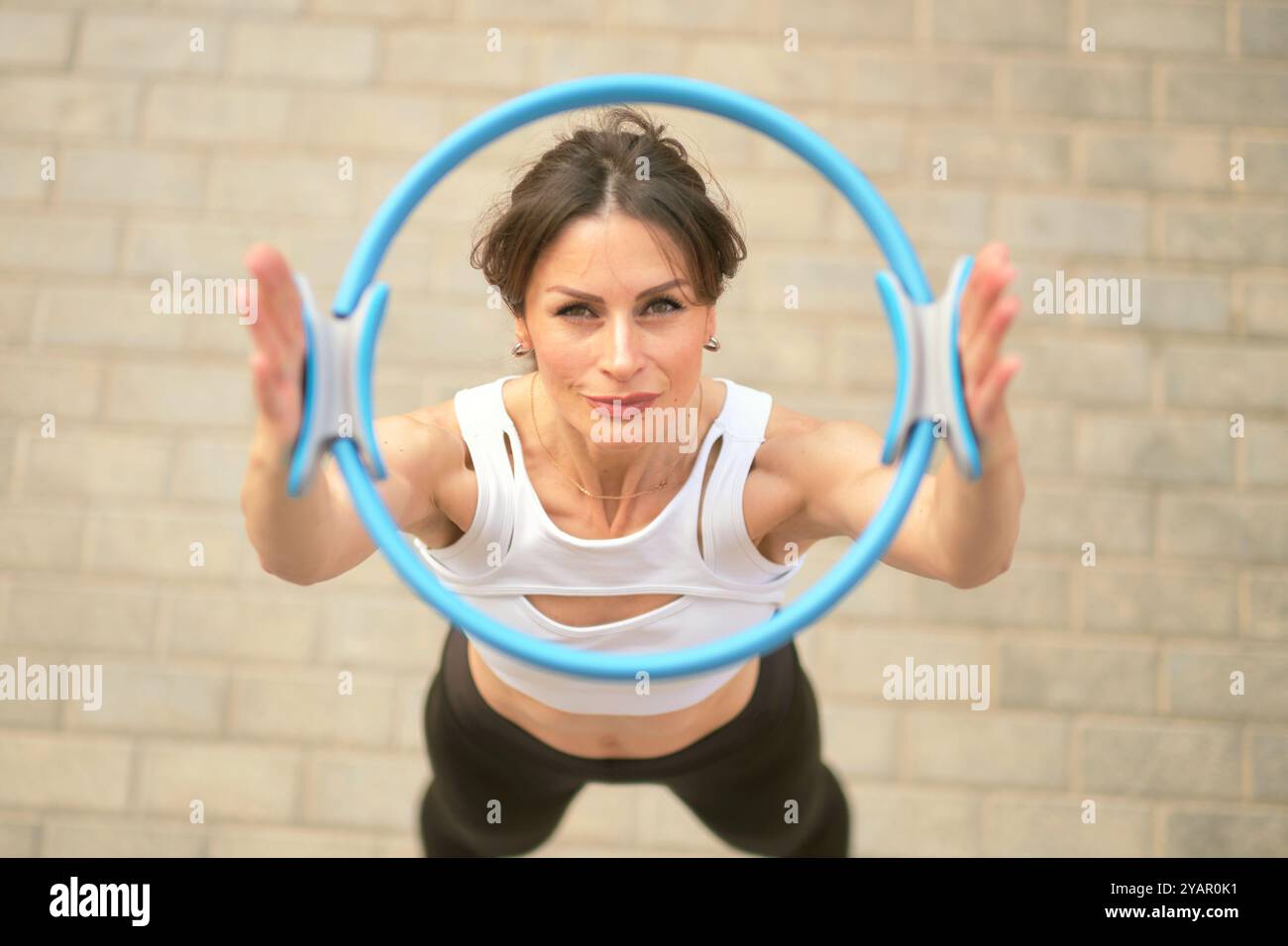 Eine fitte Frau schaut durch einen Pilates-Ring, ihr entschlossener Blick und ihre starke Haltung betonen ihr Engagement für Fitness. Diese Abbildung zeigt die Verwendung Stockfoto