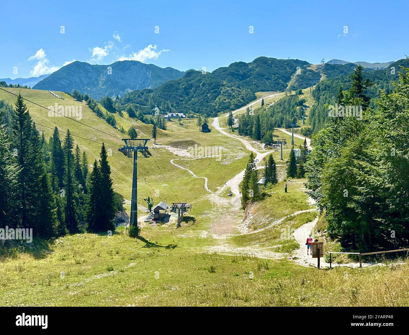 Ein Foto zeigt eine atemberaubende, sonnige Berglandschaft an einem klaren Sommertag mit üppigen grünen Hügeln und hohen Gipfeln. Stockfoto