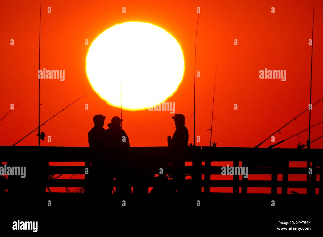 Isle Of Palms, Usa. Oktober 2024. Fisherman Silhouetten von einem dramatischen Sonnenaufgang werfen ihre Linien vor der Isle of Palms Pier am 15. Oktober 2024 in Isle of Palms, South Carolina. Für das niedere Land ist ungewöhnlich kühle Wetter vorhergesagt, bevor es später in der Woche wieder zu warmem Wetter zurückkehrt. Quelle: Richard Ellis/Richard Ellis/Alamy Live News Stockfoto