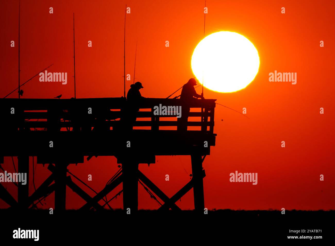 Isle Of Palms, Usa. Oktober 2024. Fisherman Silhouetten von einem dramatischen Sonnenaufgang werfen ihre Linien vor der Isle of Palms Pier am 15. Oktober 2024 in Isle of Palms, South Carolina. Für das niedere Land ist ungewöhnlich kühle Wetter vorhergesagt, bevor es später in der Woche wieder zu warmem Wetter zurückkehrt. Quelle: Richard Ellis/Richard Ellis/Alamy Live News Stockfoto