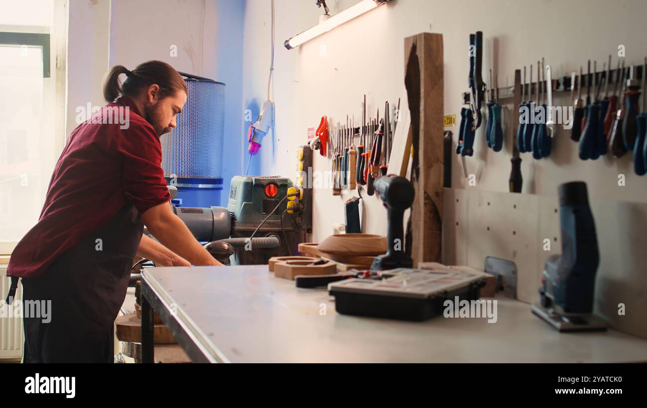Zimmermann, der das Werkzeug vom Gestell zum Einsatz auf Holzmaterialien auswählt, unterstützt von einem afroamerikanischen Kollegen. Handwerker, der Qualitätssicherung auf Holzstapel mit BIPOC-Lehrling, Kamera B, macht Stockfoto