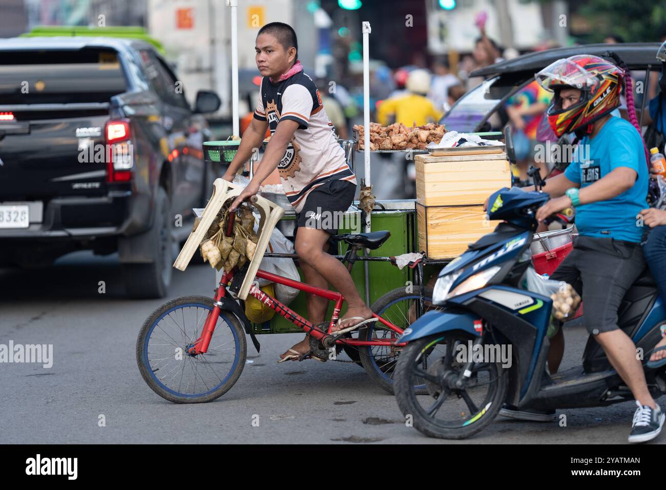 12/10/2024 Cebu City, Philippinen. Straßenverkäufer mit gebratenem Huhn, der an einer geschäftigen Kreuzung seinen mobilen Straßenkost in die Pedale fährt. Stockfoto