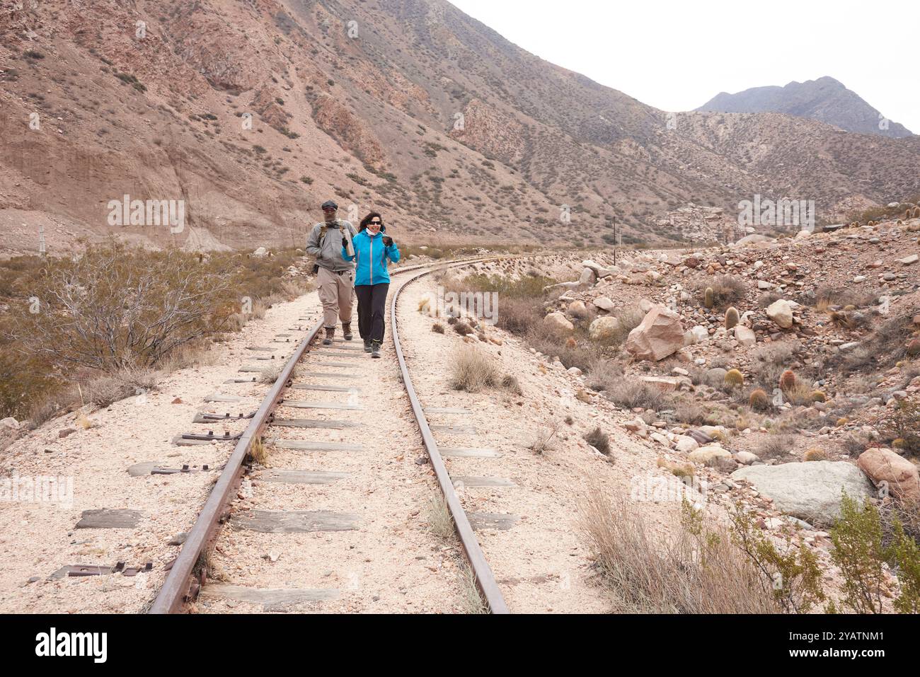 Ein paar Freunde, Mann und Frau, laufen im Winter auf den Bahngleisen in Potrerillos, Mendoza, Argentinien. Sie sind trinkende Kumpel, eine traditionelle Arge Stockfoto