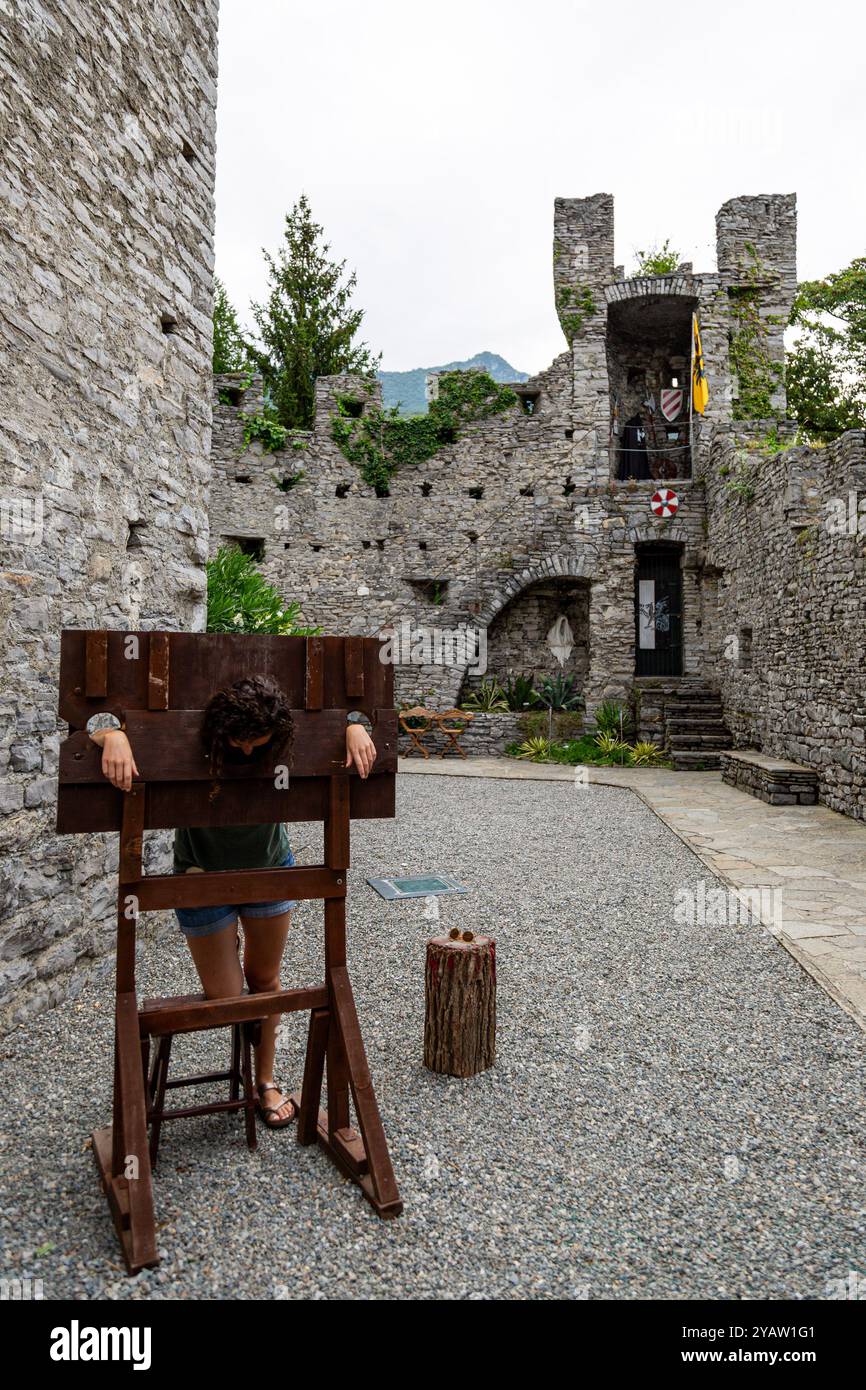 Eine Frau gibt vor, eine Gefangene in einem nachgebildeten Pranger zu sein, inmitten der Ruinen der mittelalterlichen Burg Vezio in Perledo, Lombardei, Italien. Stockfoto