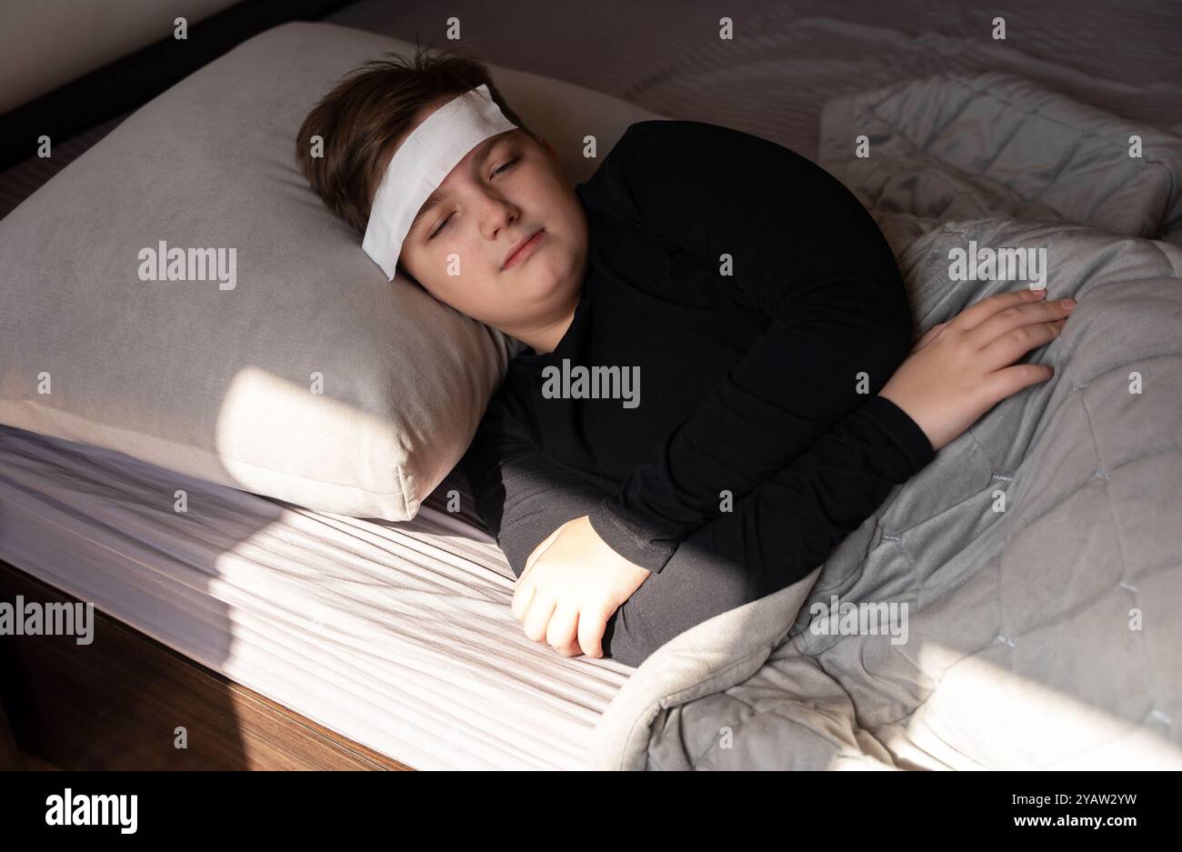 Ein 12-jähriger Junge ist krank, er liegt auf dem Bett unter einer Decke mit einem weißen nassen Tuch auf der Stirn. Stockfoto