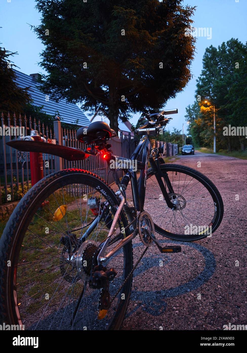 Das Mountainbike liegt in einer ruhigen Vorstadtstraße in der Abenddämmerung, beleuchtet vom Licht des Rücklichts, bereit für das nächste Abenteuer. Stockfoto