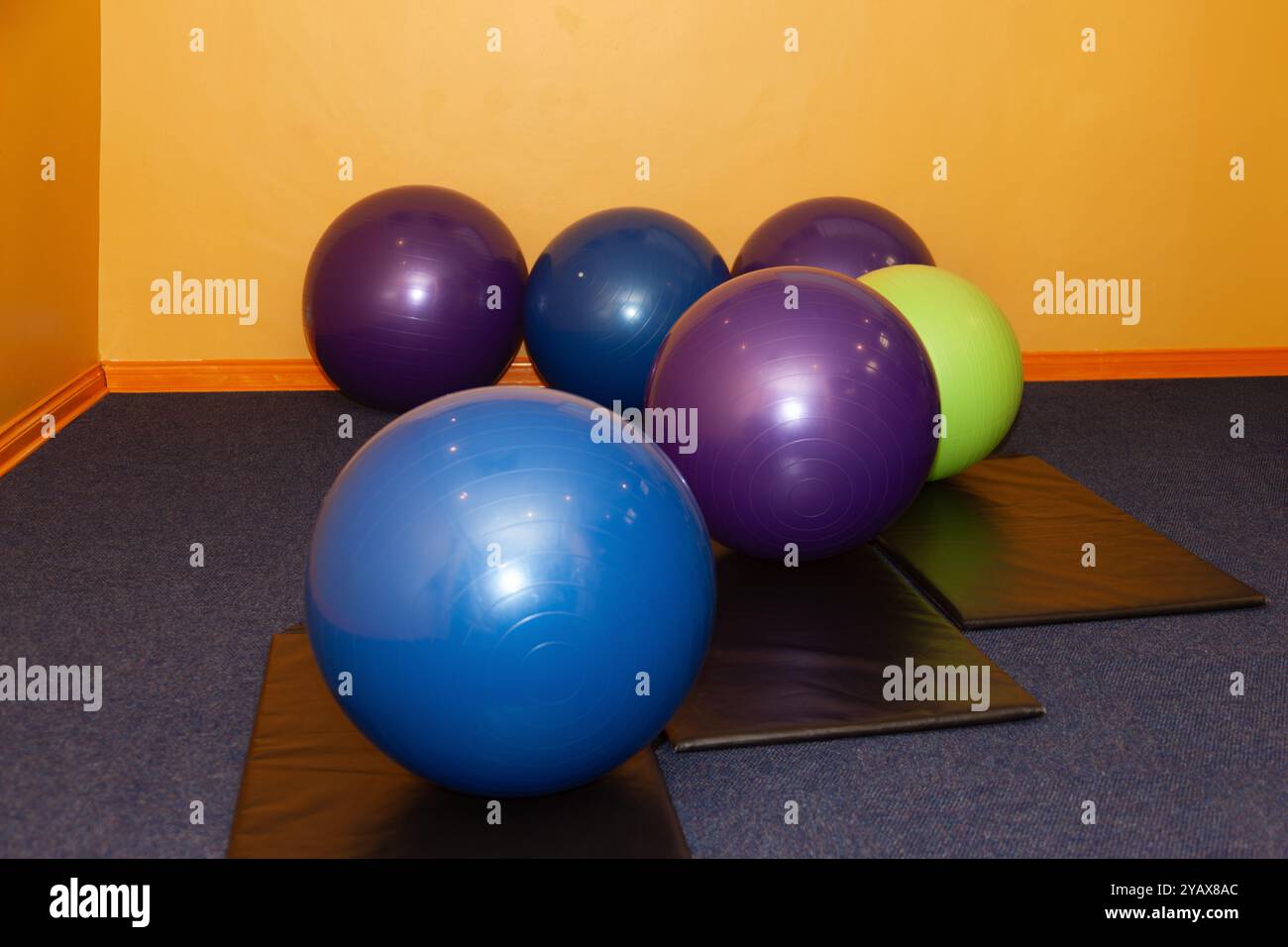 Fitnessraum-Balancebälle für Physiotherapie in verschiedenen Farben auf dem Clubboden und schwarzen Matten Stockfoto