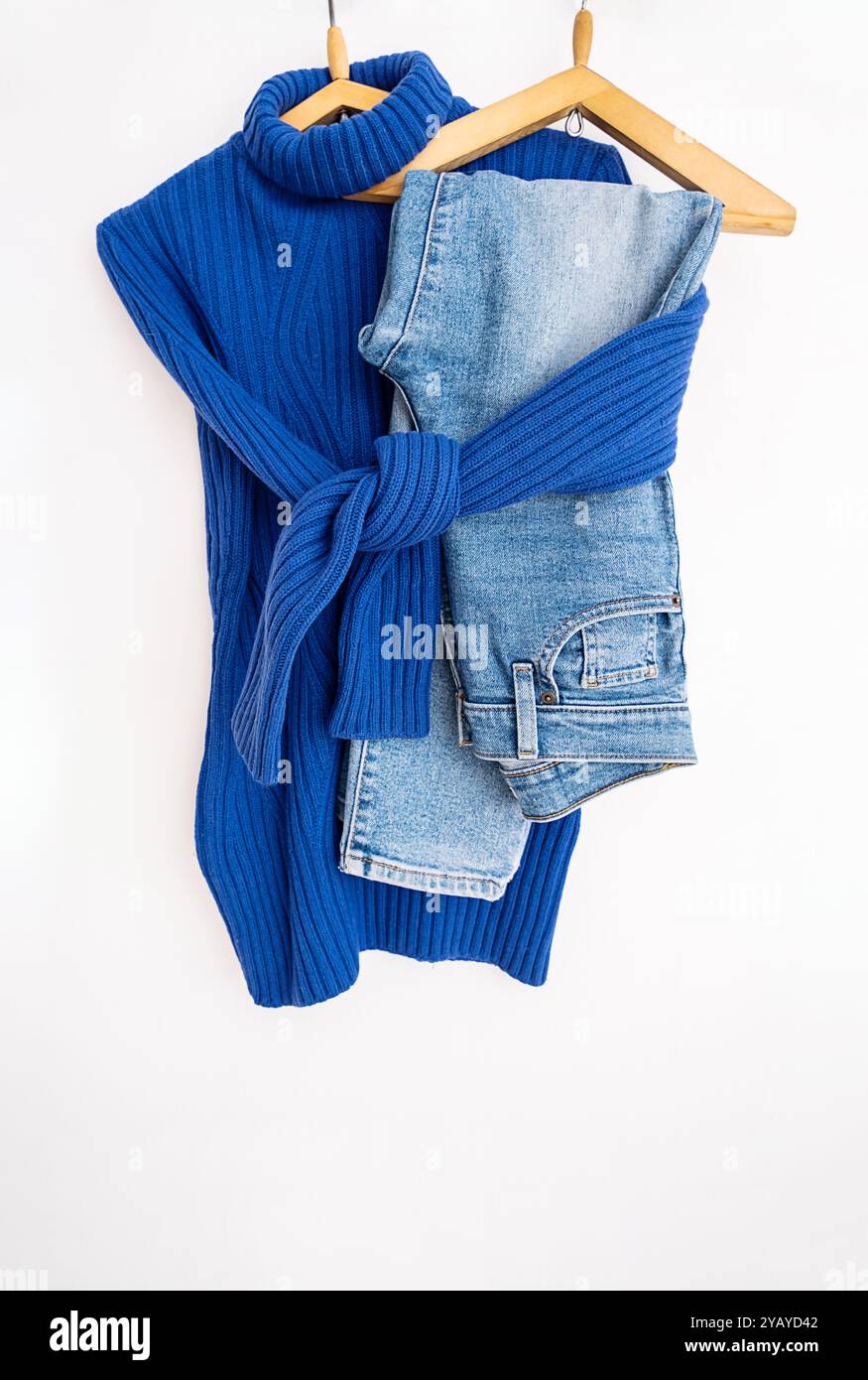 Pullover mit leuchtendem blauem Strickmuster und Denim-Jeans auf hölzernen Bügeln Stockfoto