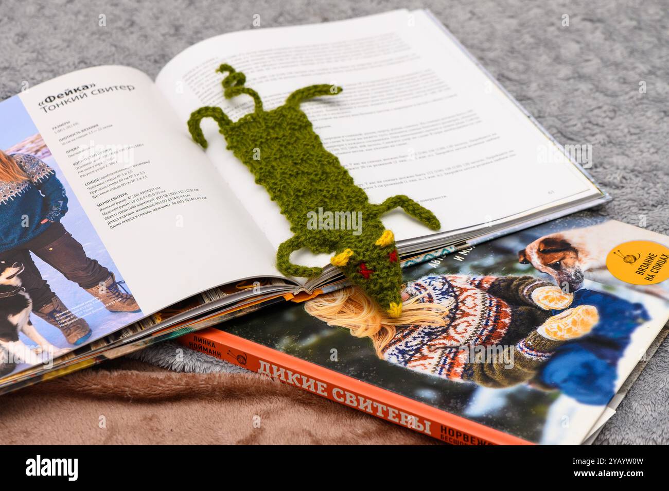 Eingebettet zwischen geöffneten Büchern liegt ein bezauberndes, gestricktes Lesezeichen, das einem verspielten Wesen ähnelt, bequem und unterstreicht einen warmen und einladenden Leseraum Stockfoto