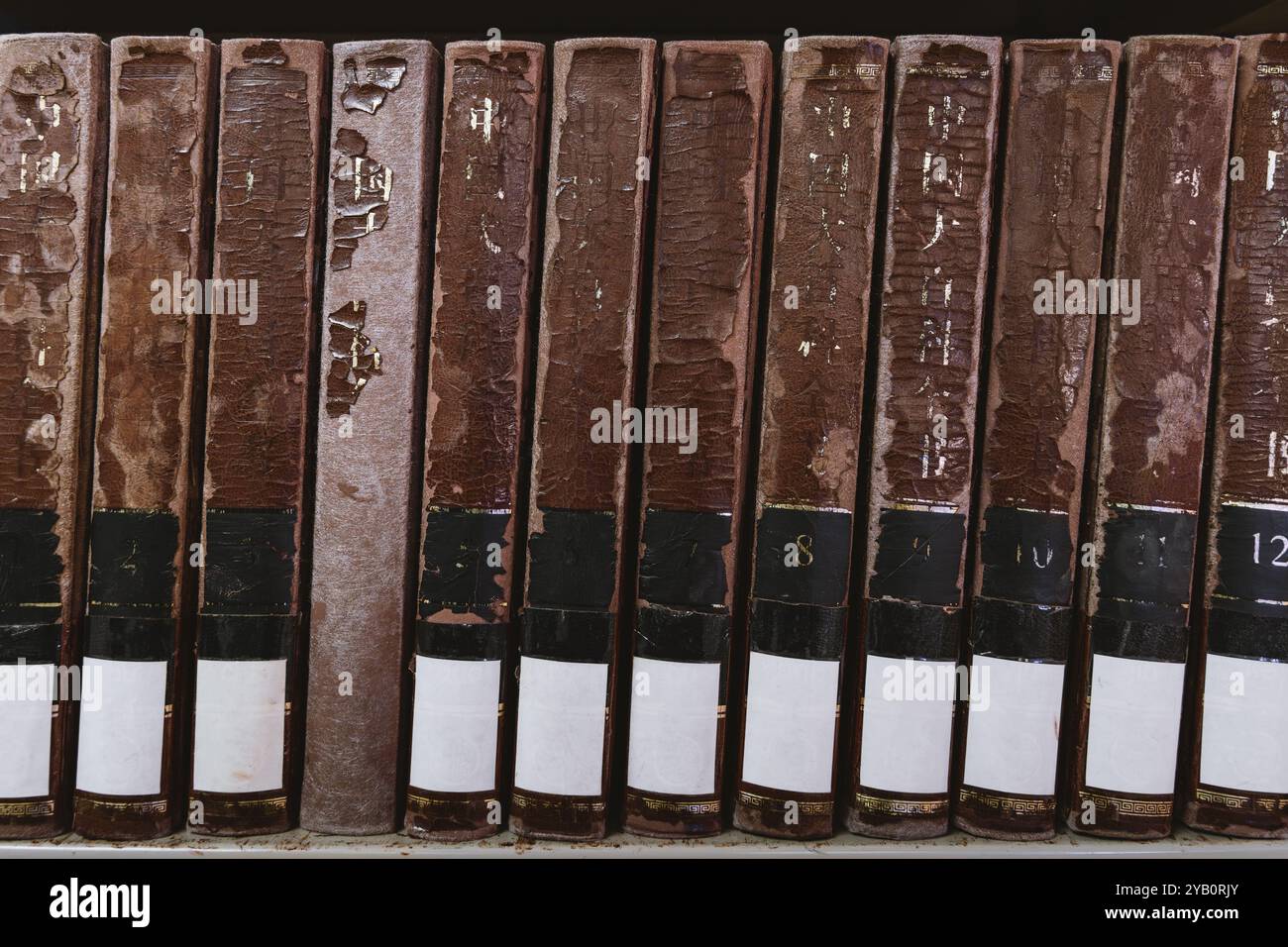 Eine Reihe alter, abgenutzter Bücher mit braunem Cover und verblasstem Text auf dem Rücken. Die Bücher sind nummeriert und zeigen Anzeichen von erheblichem Verschleiß. Stockfoto